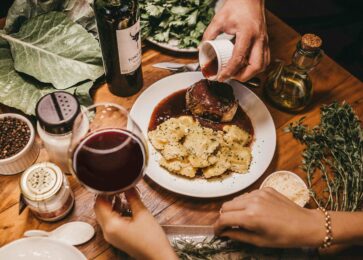 a marinated meal with a hand holding a glass of red wine