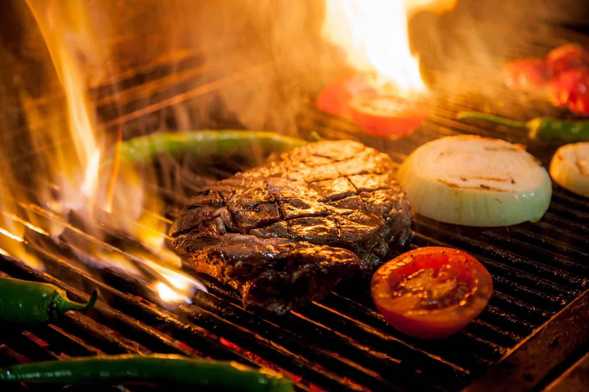 Steak cooking over an open wood fire grill with onions, tomatoes and peppers